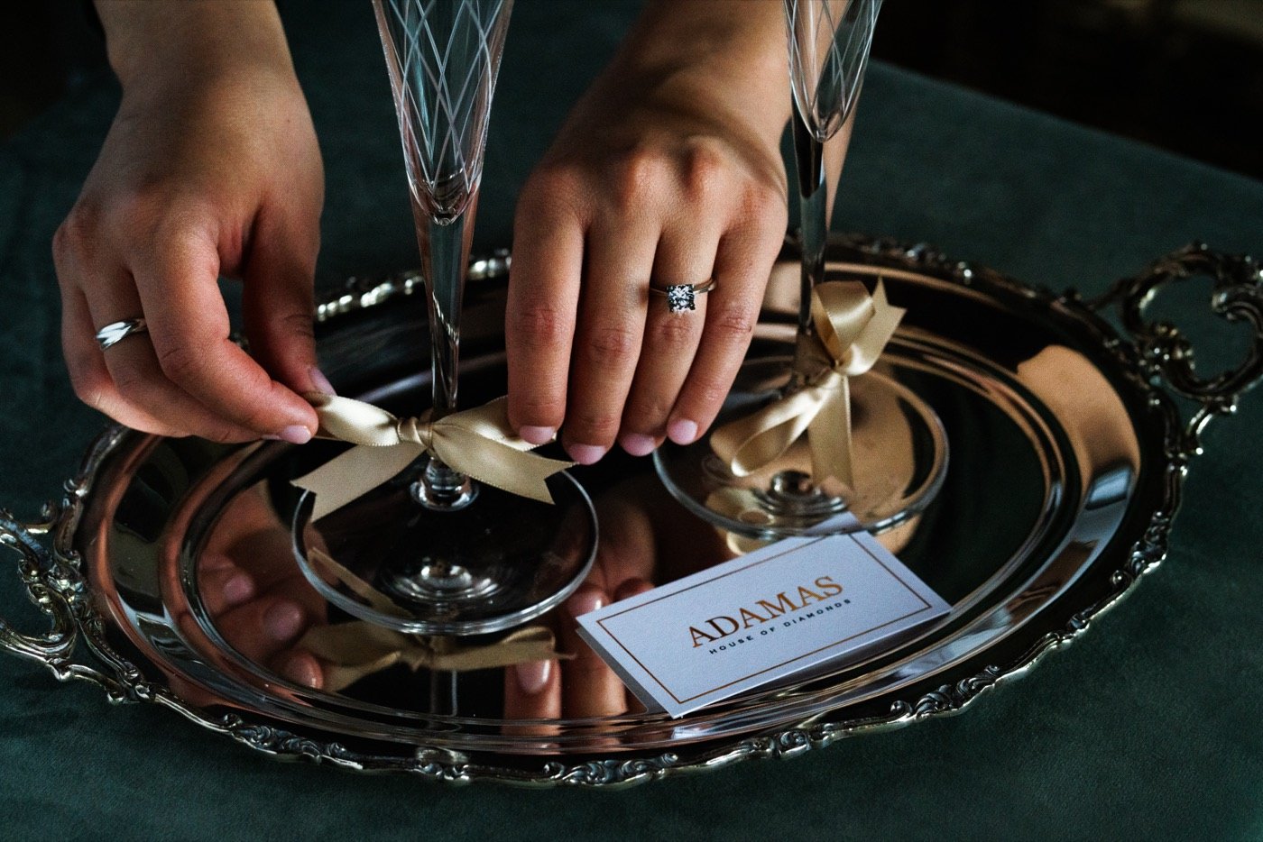 Hands tying ribbons on champagne glasses on a silver tray