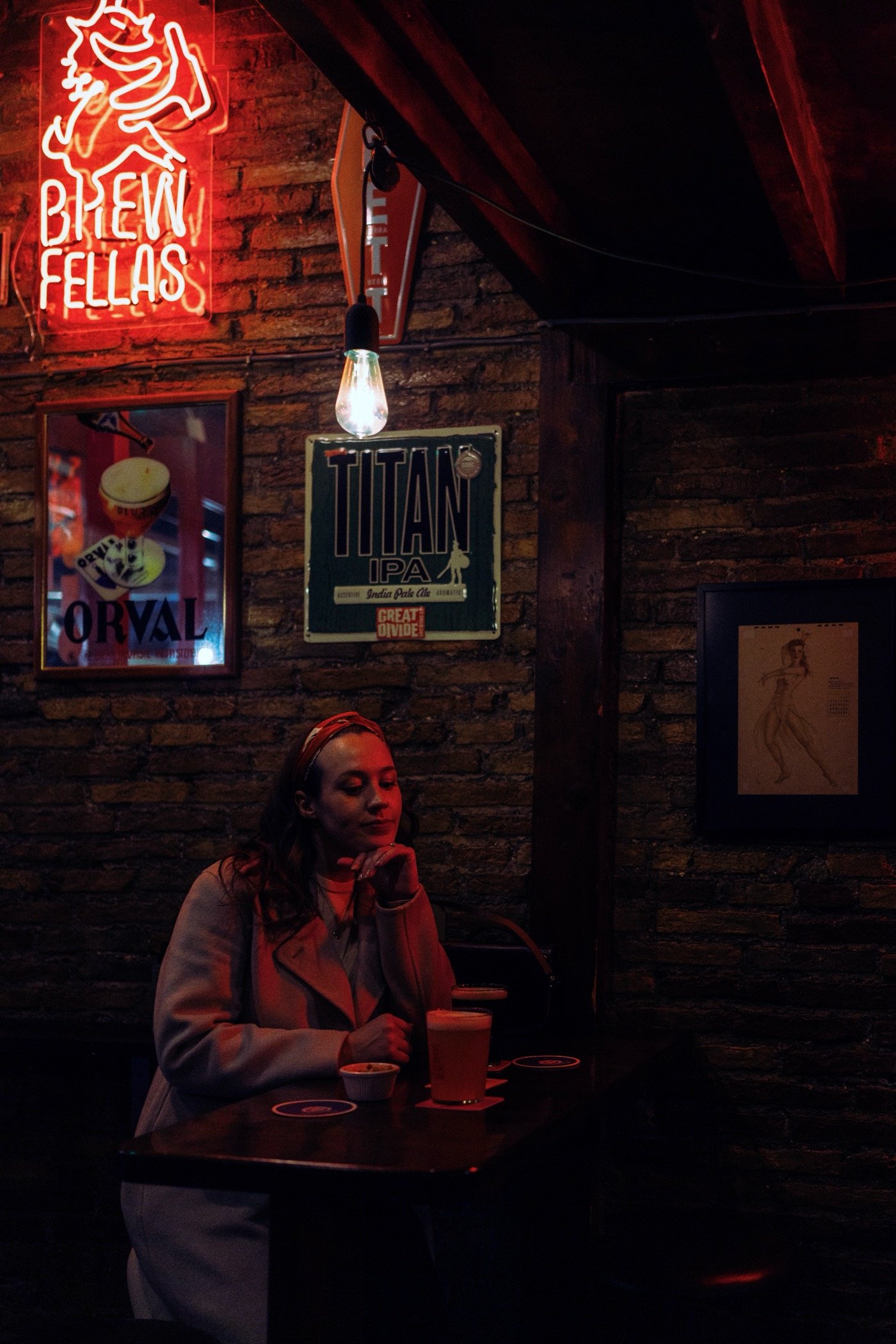 Woman sitting in a dim bar beneath a neon sign