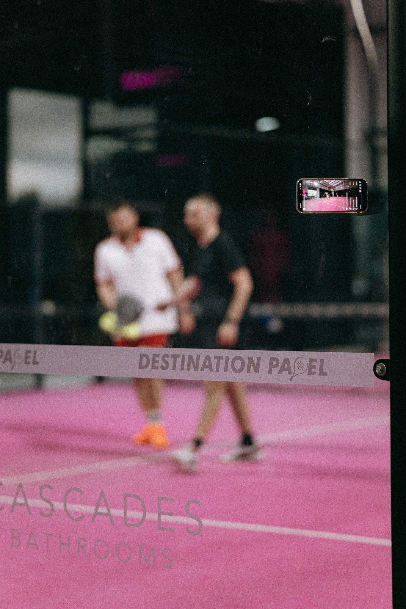 Padel players behind a Destination Padel court barrier