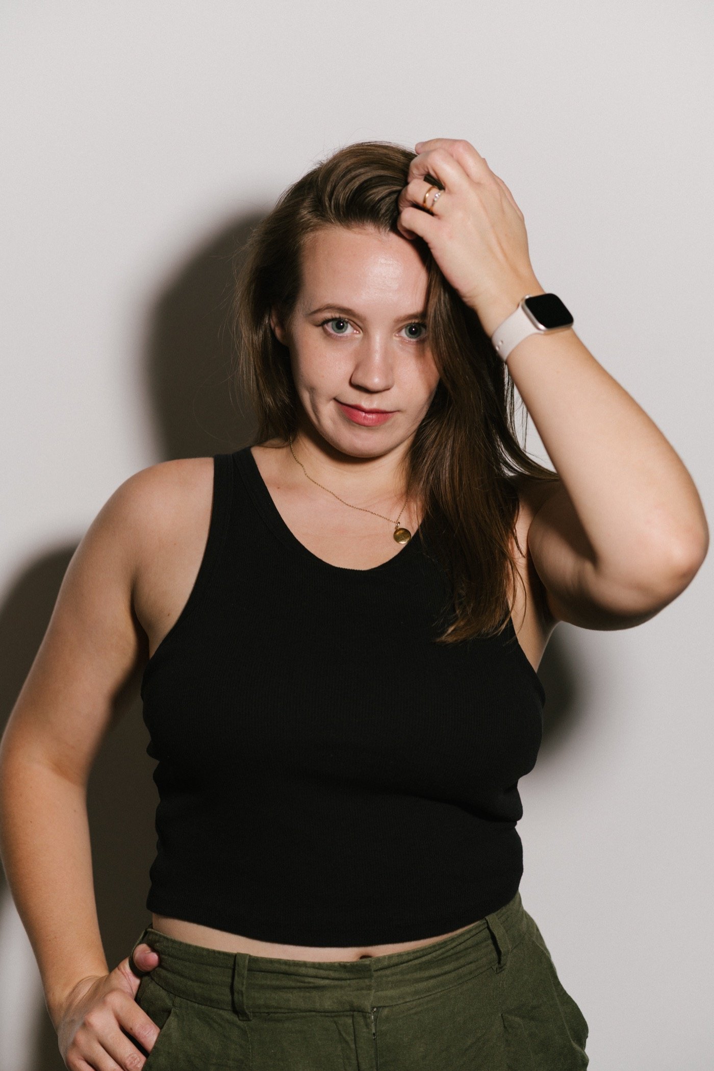 Woman in a black vest top against a white wall
