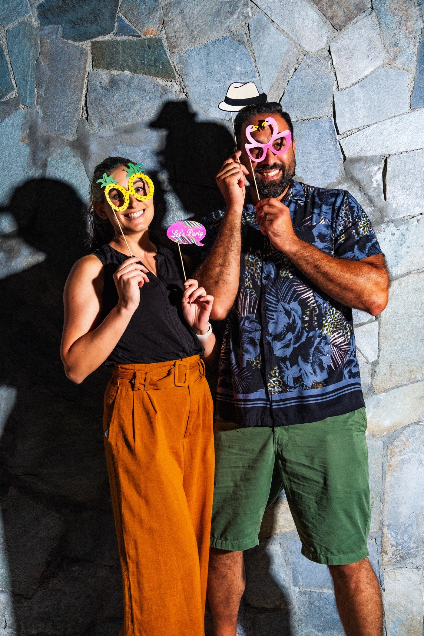 Two friends in party glasses against a stone wall