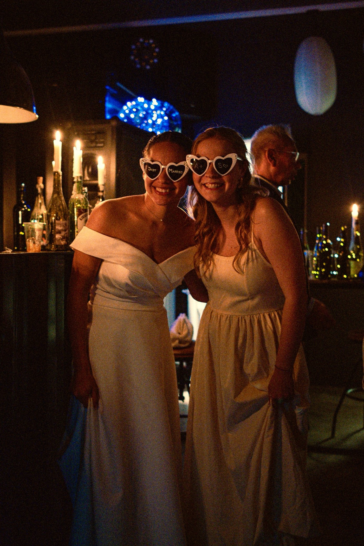 Two women in white dresses and heart-shaped sunglasses at a party