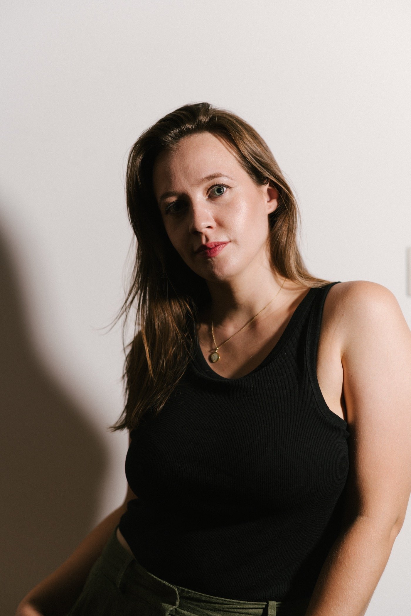 Woman in a black top leaning against a white wall