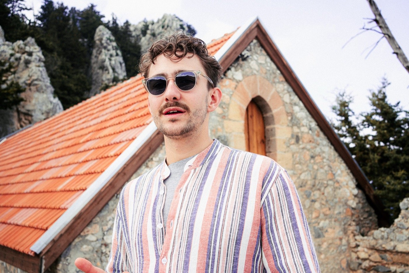 Man in a striped shirt and sunglasses by a stone chapel